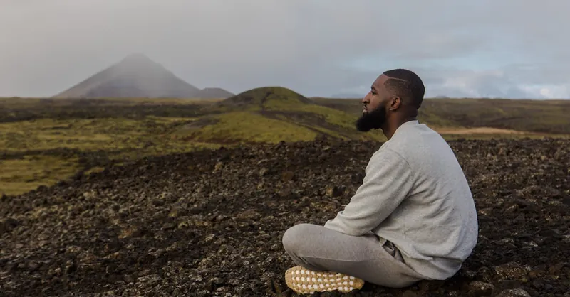 Man meditating on rocky terrain with mountain backdrop. Peace and tranquility outdoors.