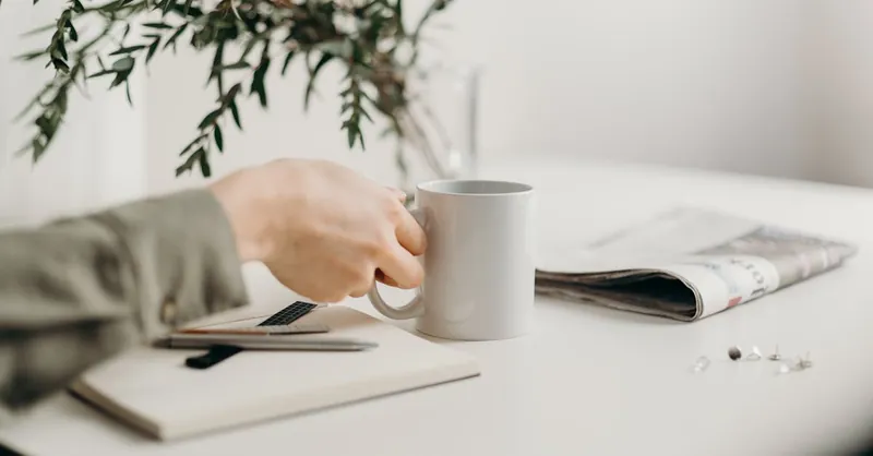 A minimalist workspace featuring a mug, notebook, and greenery, perfect for productivity.