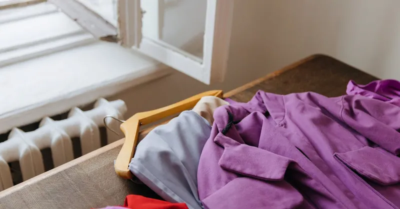 Purple coat on hanger beside open window, offering natural light and warmth.