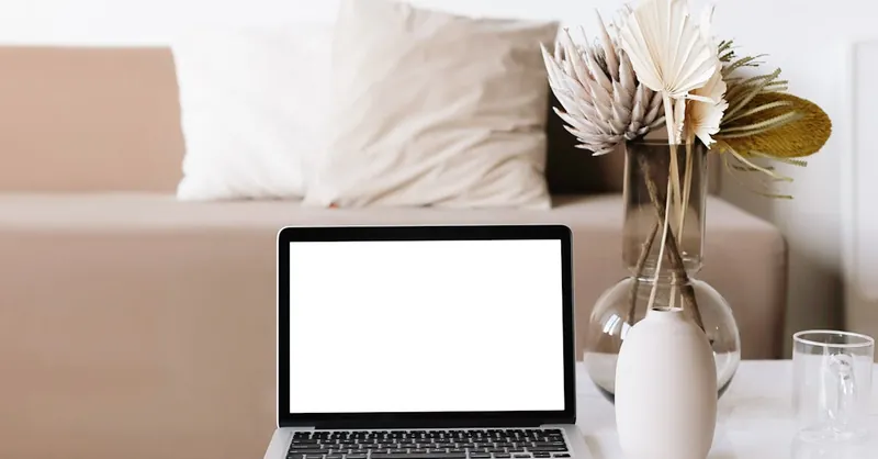 A minimalist workspace setup in a living room with a laptop, vase, and neutral tones.