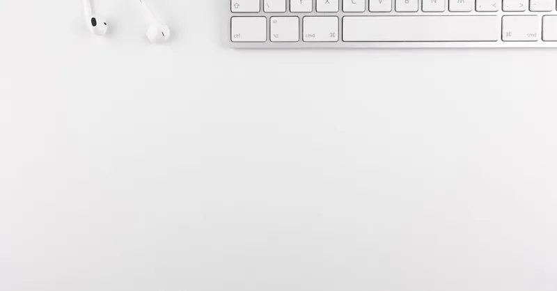 Top view of a white minimalist desk featuring a keyboard and earphones, ideal for technology themes.