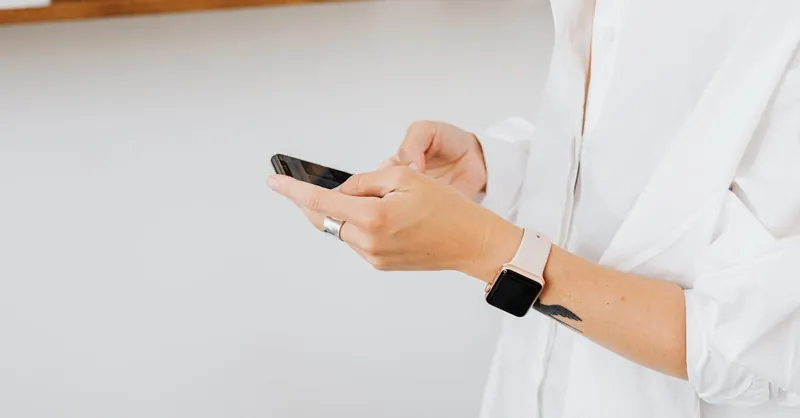 Close-up of person in white shirt using smartphone, wearing a smartwatch.