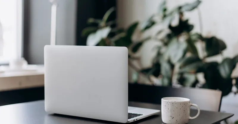 A minimalist workspace featuring a closed laptop and a coffee cup on a table, offering a serene and focused atmosphere.