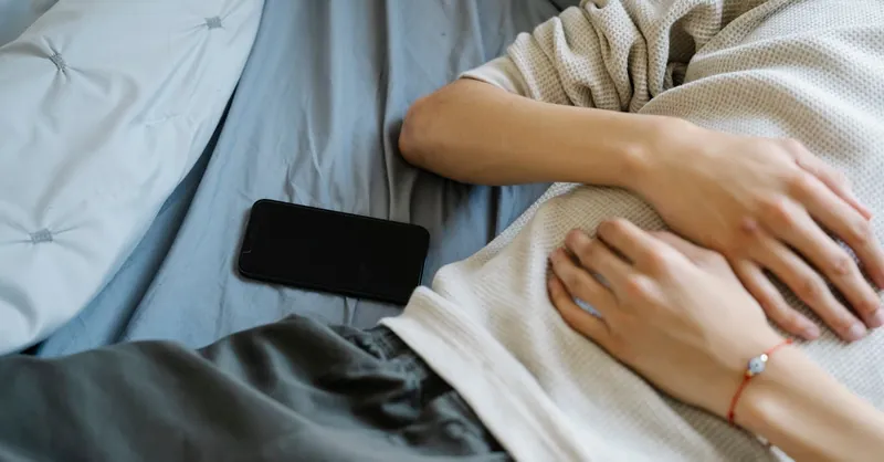 A young adult lying on a bed next to a smartphone, capturing a moment of relaxation and technology use.