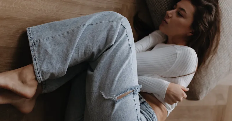 Woman in casual clothing lying on wooden floor, conveying vulnerability and introspection.