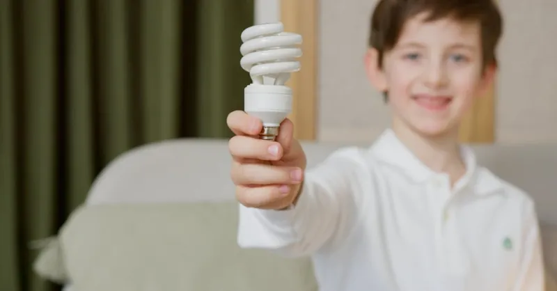 Young boy with light bulb promoting energy efficiency indoors.