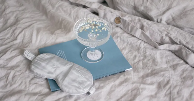 A relaxing setup with a sleep mask, book, and glass flowers on a bed.