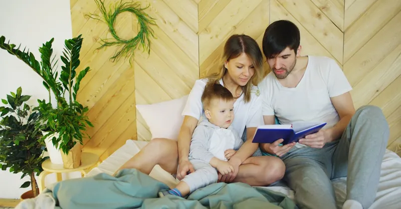 Loving parents reading a book with their child in a cozy bedroom setting, promoting family bonding.