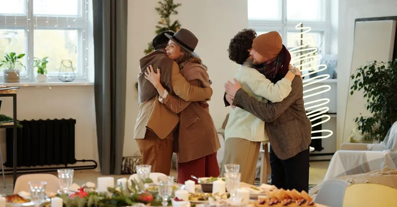 A joyful indoor holiday celebration with family and friends embracing around the dining table.