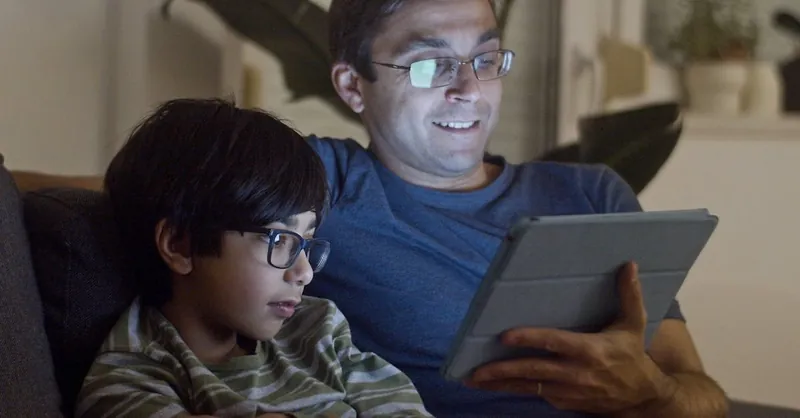 A father and son enjoy quality time using a tablet together indoors, creating a warm and intimate moment.