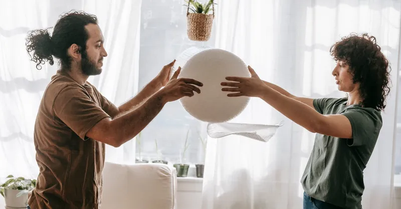 A couple collaborates in packing household items with bubble wrap, showcasing teamwork and organization indoors.