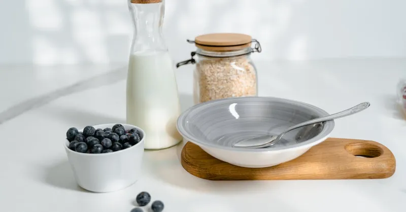 A minimalistic breakfast setup featuring blueberries, milk, and oats on a bright kitchen counter.
