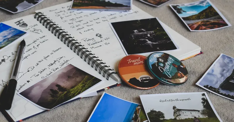 Travel diary surrounded by printed photos and a pen, capturing memories creatively.