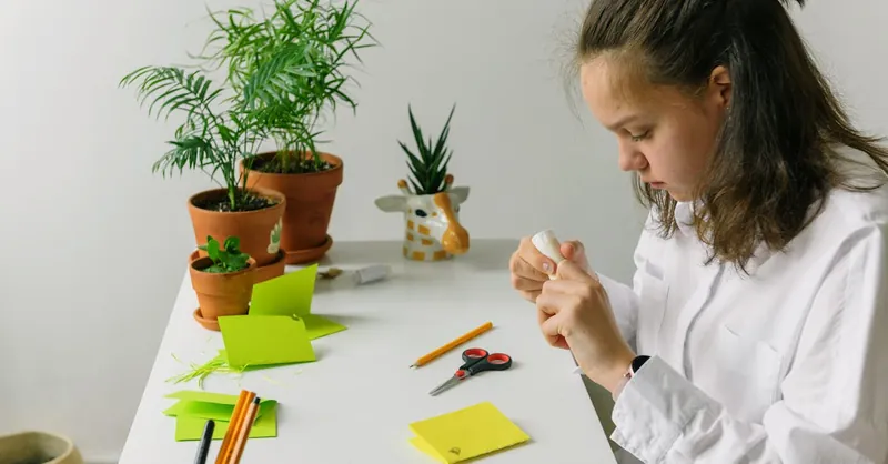 A young woman engaged in a crafting project surrounded by potted plants indoors.