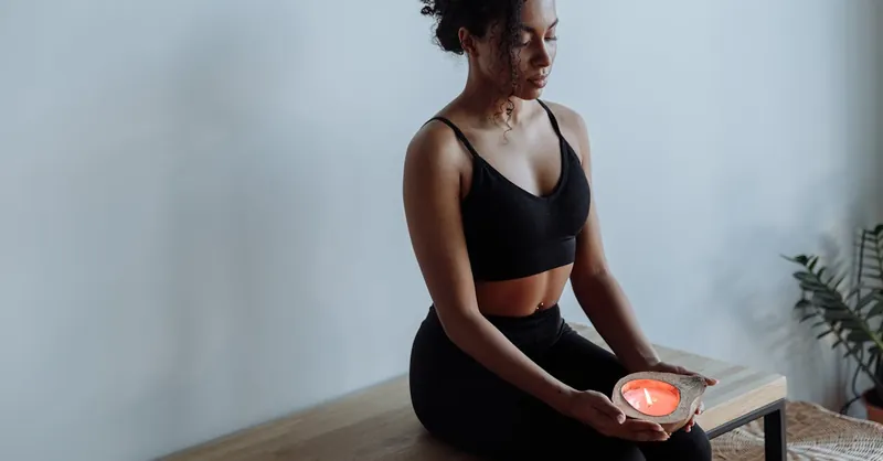 A woman in black activewear meditates with a candle, seated indoors for mindfulness and relaxation.