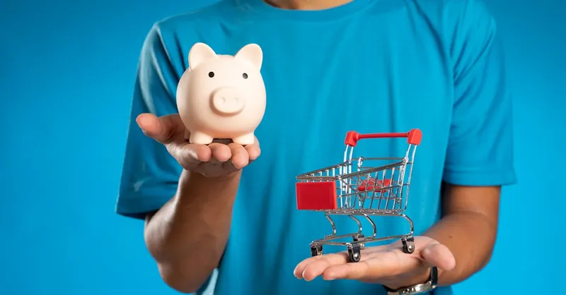 Man in blue shirt holding piggy bank and mini shopping cart, symbolizing savings versus spending.