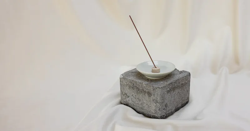 A serene minimalist setup featuring an incense stick in a holder on a stone block, perfect for promoting calm and inner peace.
