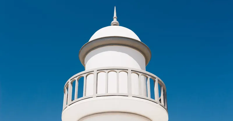 A minimalist white lighthouse tower stands tall against a perfect clear blue sky, showcasing modern architecture.