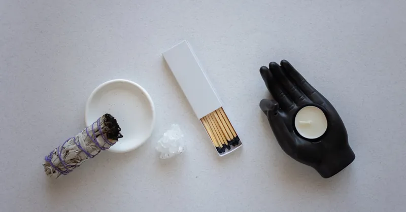A top view of spiritual decor with a candle, sage bundle, and matches on a minimalist background.
