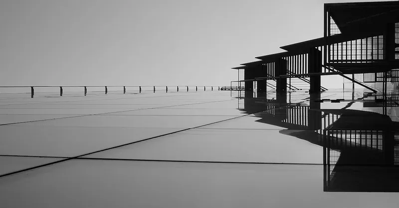 A striking minimalist black and white image featuring architectural reflections on glass surfaces.