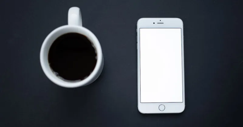 Minimalist composition featuring a smartphone next to a coffee mug on a dark surface.