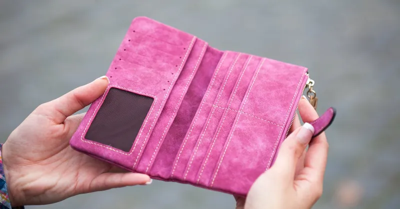 A woman holds an open, empty pink wallet outdoors, emphasizing financial themes.