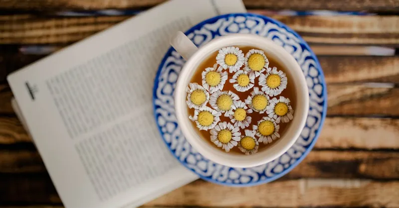 Overhead shot of chamomile tea in a decorative cup with an open book, exuding a calm and cozy vibe.