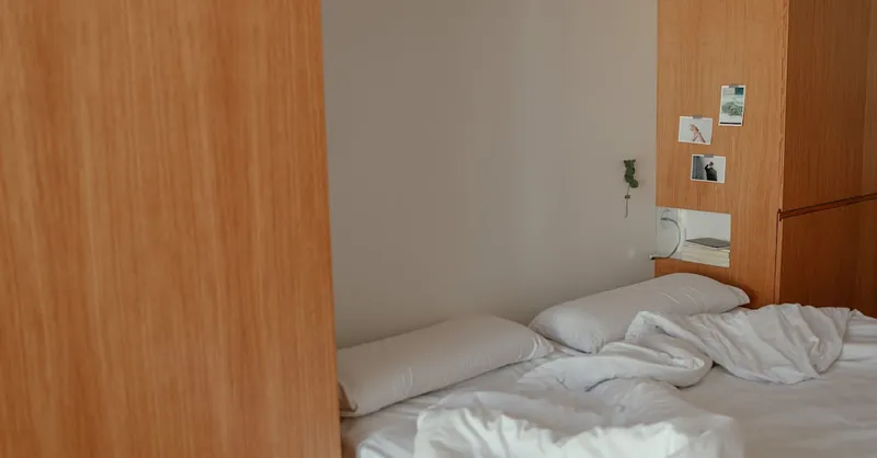A serene minimalist bedroom featuring white linens and wooden decor elements.