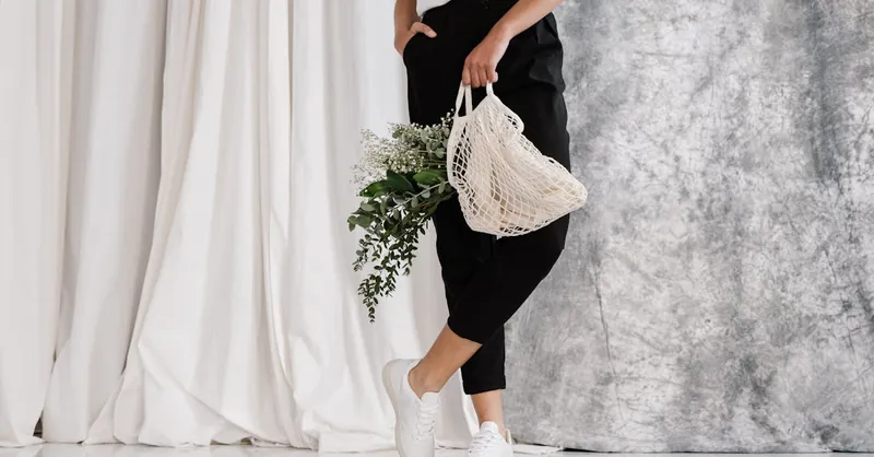 Adult holding eco-friendly mesh bag with green foliage against minimalist backdrop.
