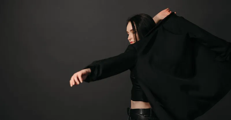 Elegant woman putting on a black blazer in a minimal studio setting, showcasing modern fashion.