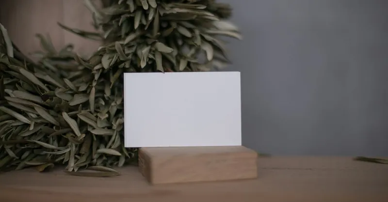 A minimalist business card on a wooden stand surrounded by olive leaves, offering ample copy space.