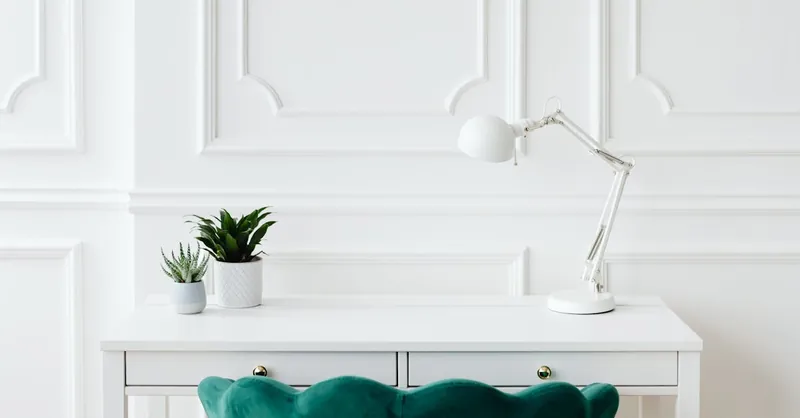 Aesthetic minimalist desk setup featuring potted plants and a white desk lamp against elegant wall paneling.