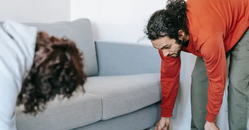 A couple tidying up their living room, organizing furniture and rugs with teamwork.