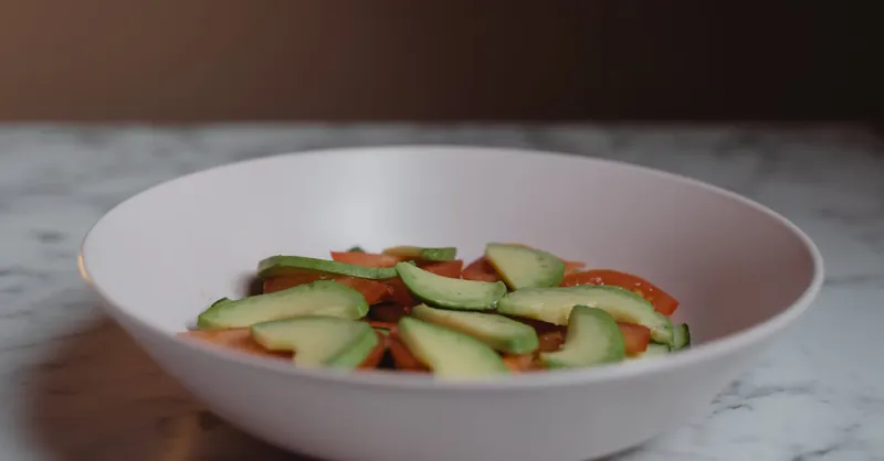 A delicious vegan salad featuring sliced avocado and tomatoes on a marble table.