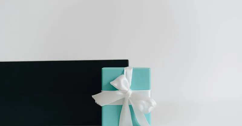 A minimalist image of a turquoise gift box adorned with a white ribbon, set against a plain background.