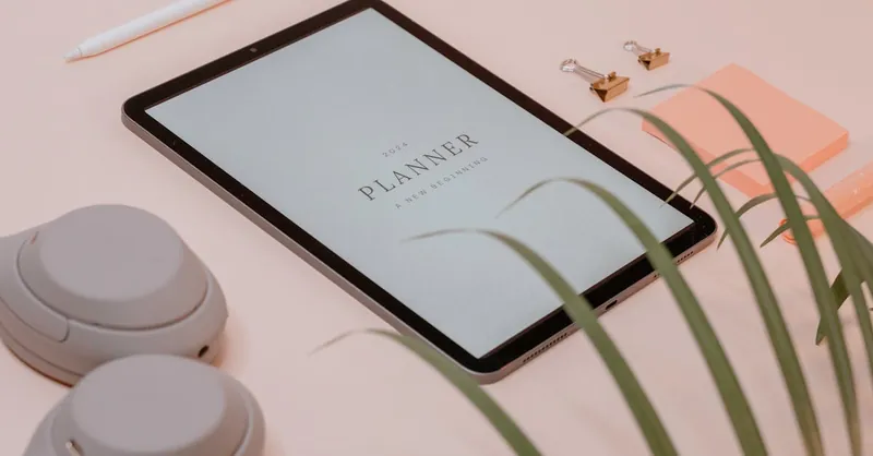A flat lay of a minimalist desk setup featuring a tablet displaying a planner for new resolutions.