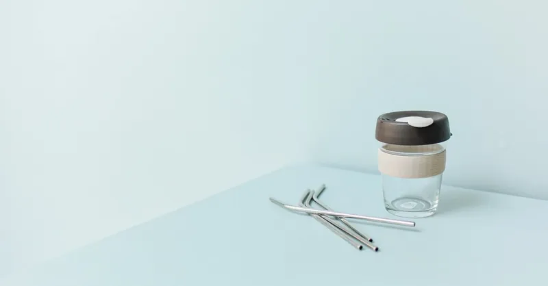 Minimalist image of a reusable cup with metal straws on a blue background, perfect for eco-friendly themes.