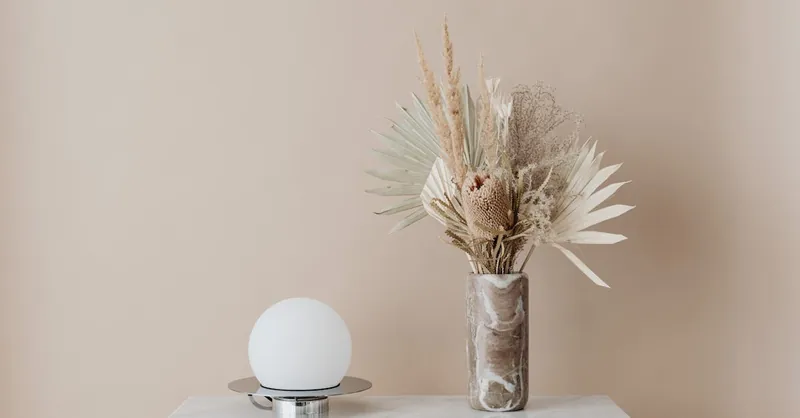 A minimalist decor arrangement featuring a vase with dried botanicals and a modern lamp on a table.