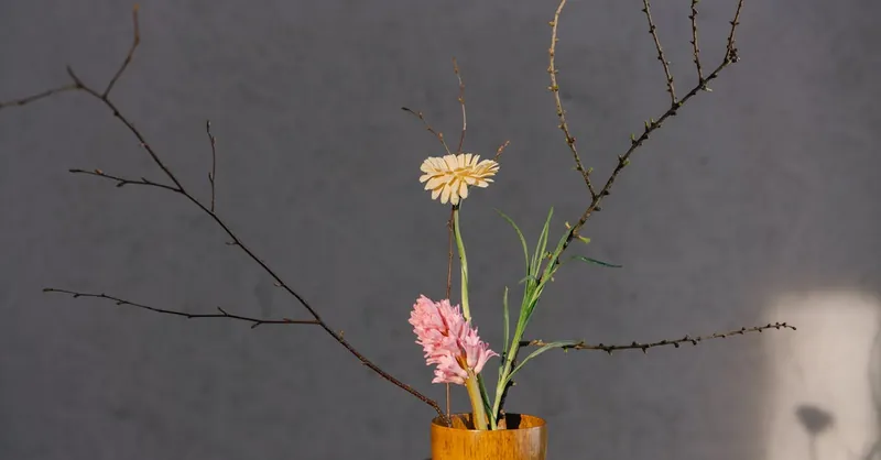 A minimalist floral arrangement in a wooden vase with branches and soft lighting.