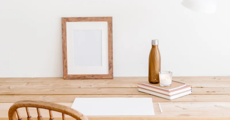 Minimalist workspace featuring a wooden chair, desk, frame, and bottle. Perfect for a calm office setting.