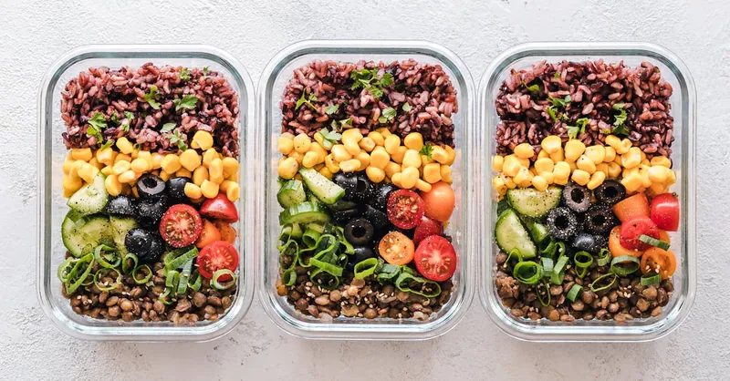 Colorful healthy meal prep with corn, olives, tomatoes, and lentils in glass containers. Perfect for mindful eating.