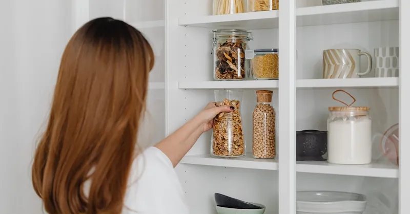Woman arranging jars on pantry shelves for organized food storage.