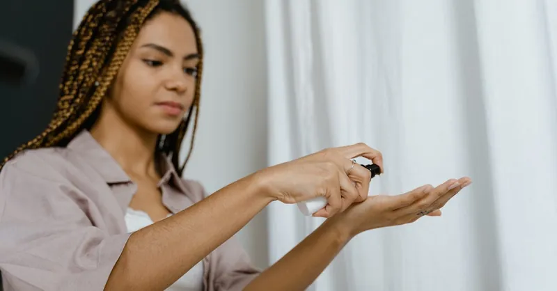 A young woman with braided hair applying a skincare product indoors, focusing on self-care.