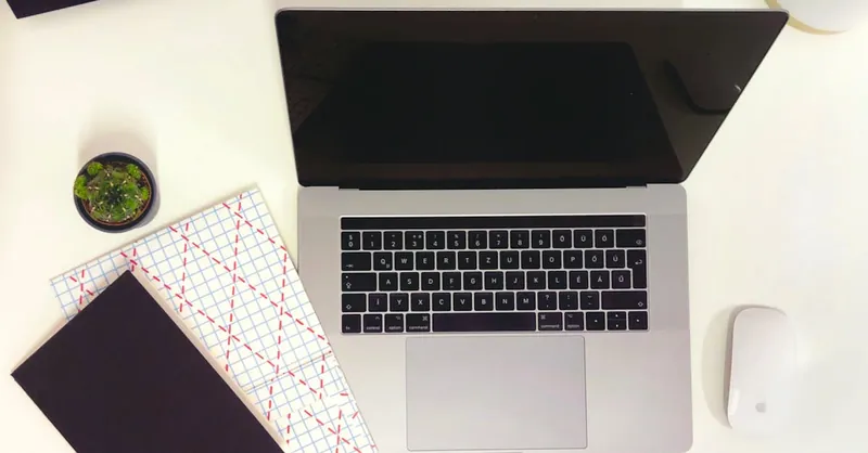 Minimalist workspace featuring a laptop, notepads, and a mouse in Budapest.
