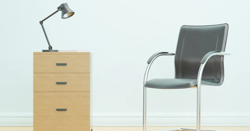 A minimalist office setup showcasing a sleek chair and wooden drawer unit with a desk lamp.