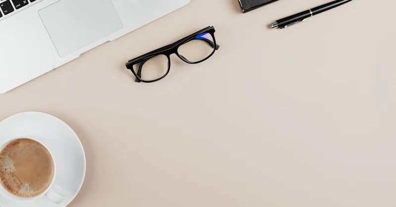 Minimalist workspace setup with laptop, coffee, and eyeglasses.