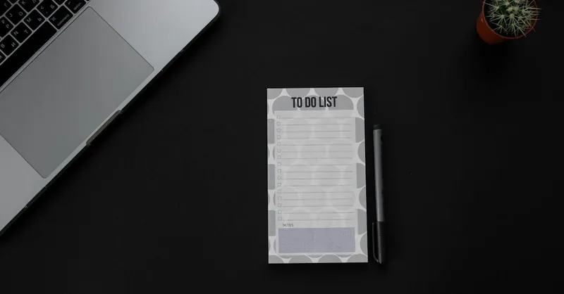 A minimalistic desk setup featuring a laptop, to-do list, and pen on a dark background. Ideal for productivity themes.