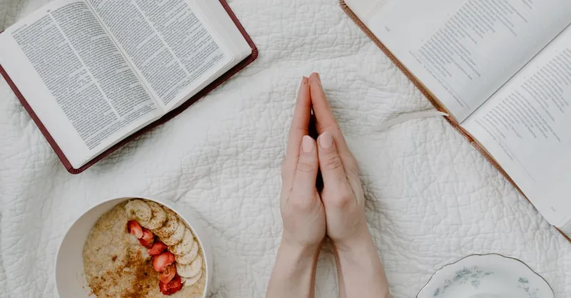 A serene morning scene with a person praying, an open Bible, oatmeal, and coffee.