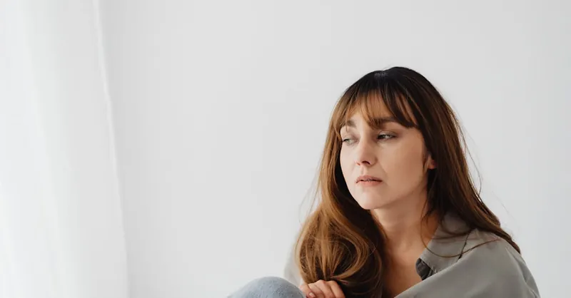 A contemplative woman sits in a minimalist white room, exuding a serene and introspective aura.