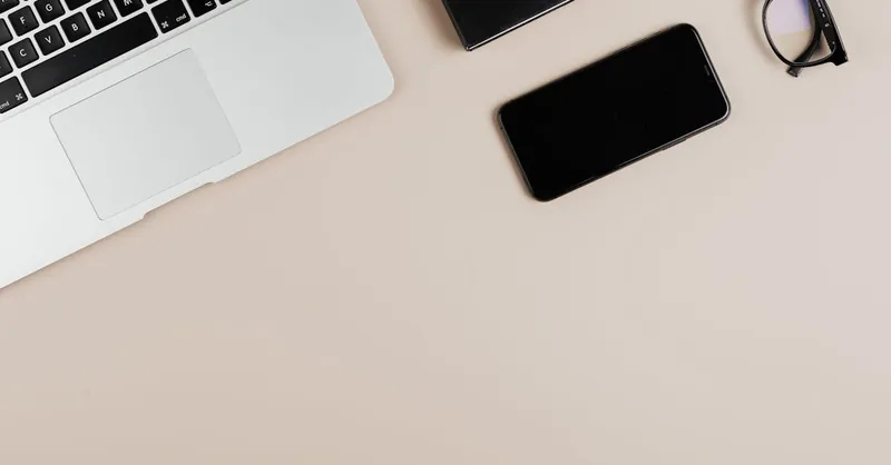 Modern workspace with laptop, smartphone, and eyeglasses on a beige surface. Ideal for tech or productivity themes.